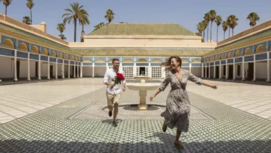 Couple running joyfully through Bahia Palace courtyard in Marrakech with the groom holding red roses — a honeymoon in Morocco blends romance with centuries of history