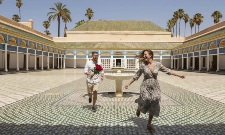 Couple running joyfully through Bahia Palace courtyard in Marrakech with the groom holding red roses — a honeymoon in Morocco blends romance with centuries of history