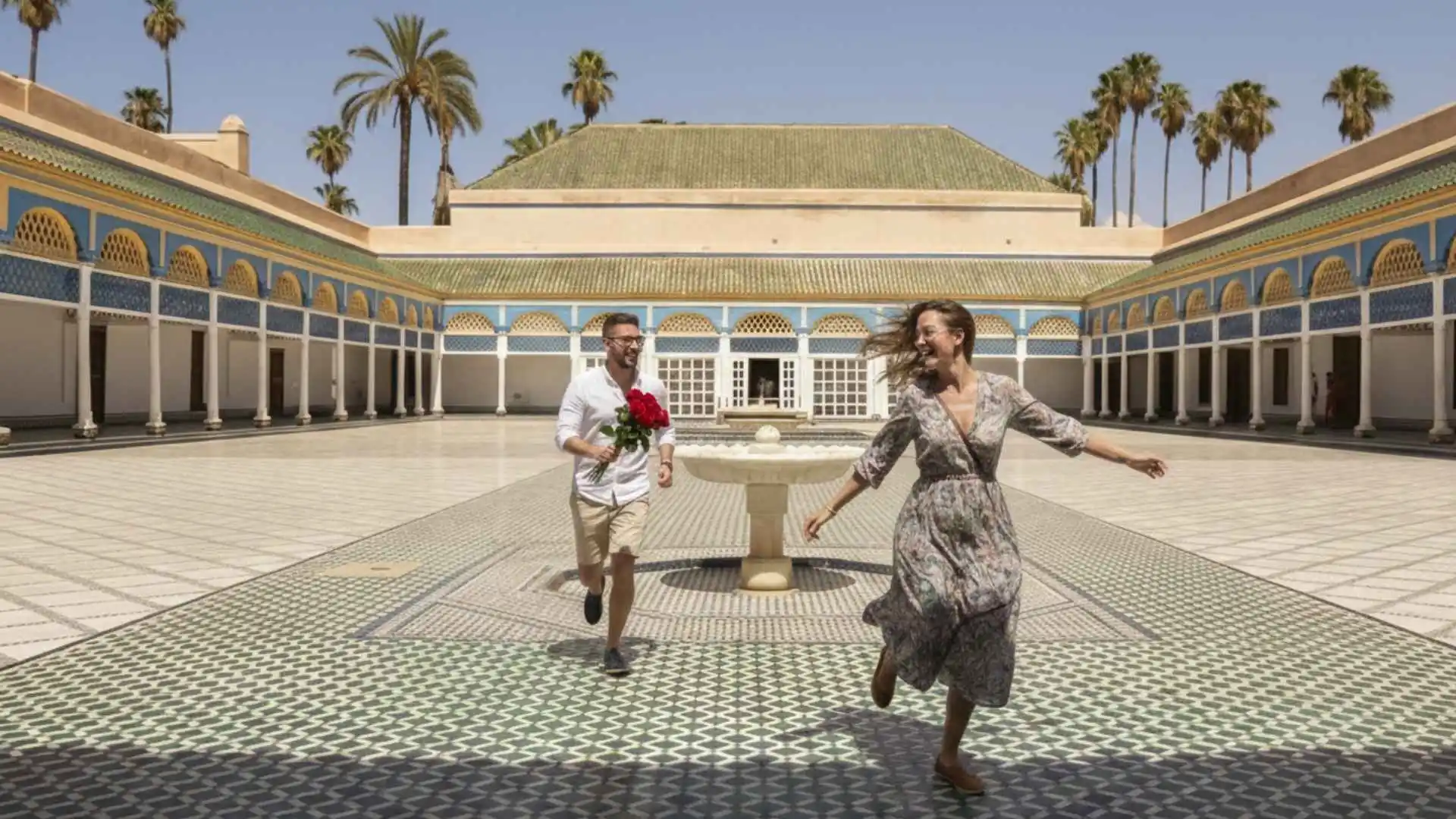 Couple running joyfully through Bahia Palace courtyard in Marrakech with the groom holding red roses — a honeymoon in Morocco blends romance with centuries of history