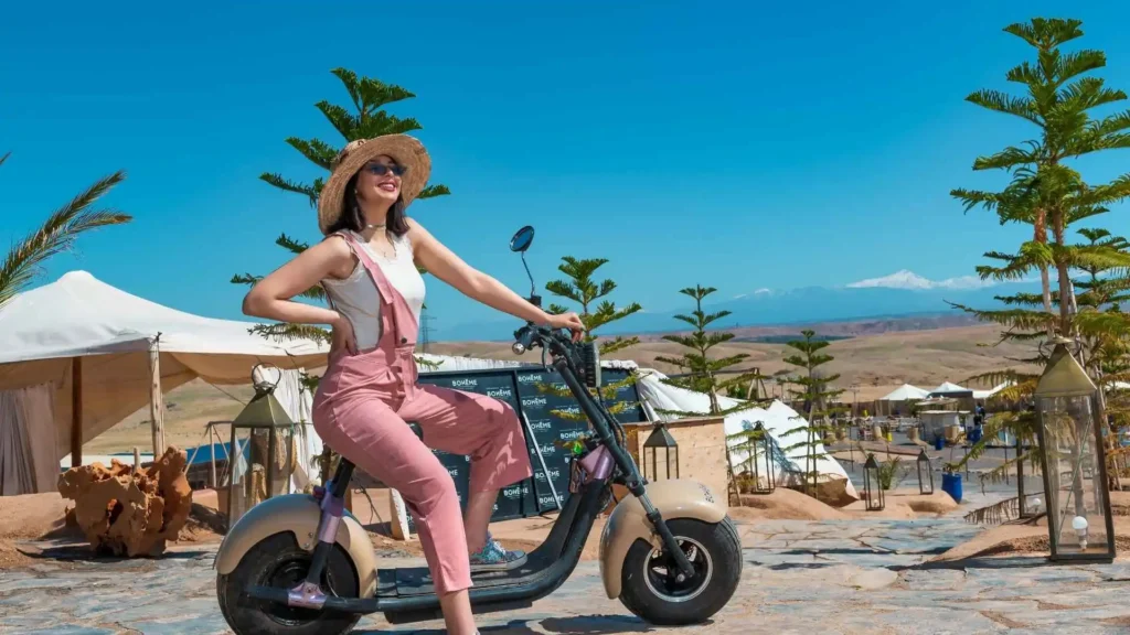 Solo female tourist posing on a scooter at a glamping resort in Morocco with the Atlas Mountains in the background, showing that Morocco is safe for Americans including women traveling alone