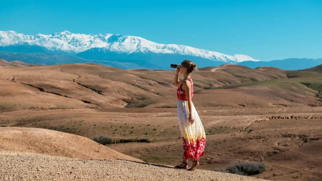 Traveler photographing the rocky Agafay Desert landscape with snow-capped Atlas Mountains in the background near Marrakech Morocco