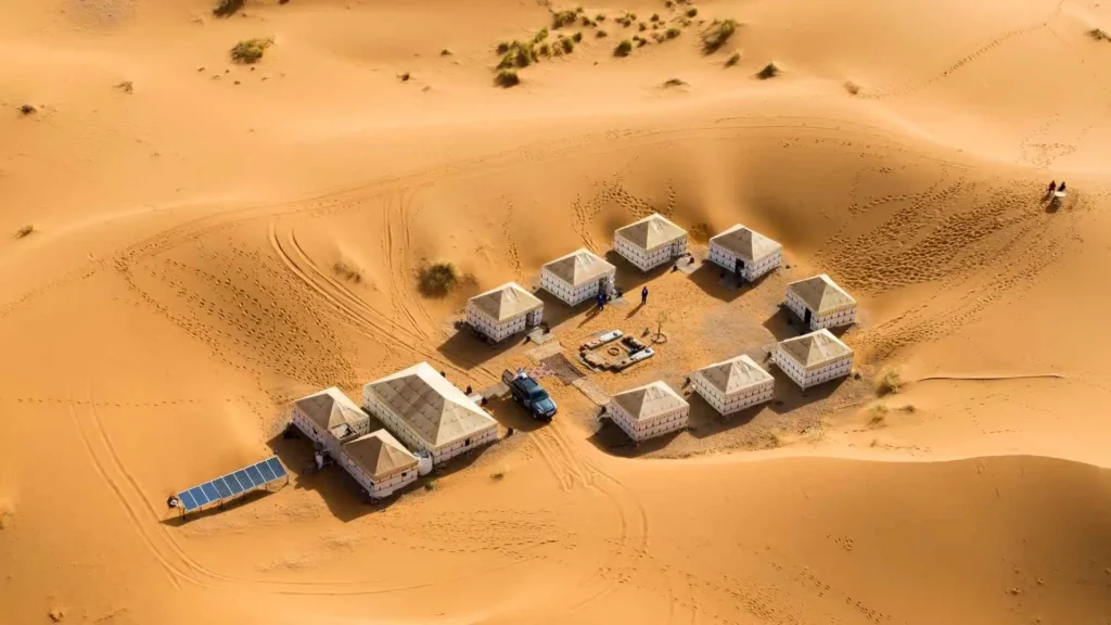 Aerial view of a Merzouga luxury desert camp with private tents and solar panels nestled among Erg Chebbi sand dunes Morocco