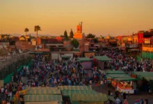 Aerial evening view of Jemaa el-Fna square in Marrakech packed with crowds and food stalls at sunset with the Atlas Mountains on the horizon — the ultimate guide to the best time to visit Morocco in 2026