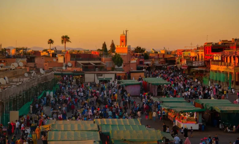Aerial evening view of Jemaa el-Fna square in Marrakech packed with crowds and food stalls at sunset with the Atlas Mountains on the horizon — the ultimate guide to the best time to visit Morocco in 2026