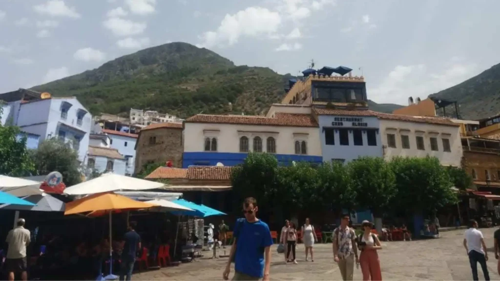 Tourists in Chefchaouen's main square with the Rif Mountains in the background — the best time to visit Morocco's blue city is April to May or September to October