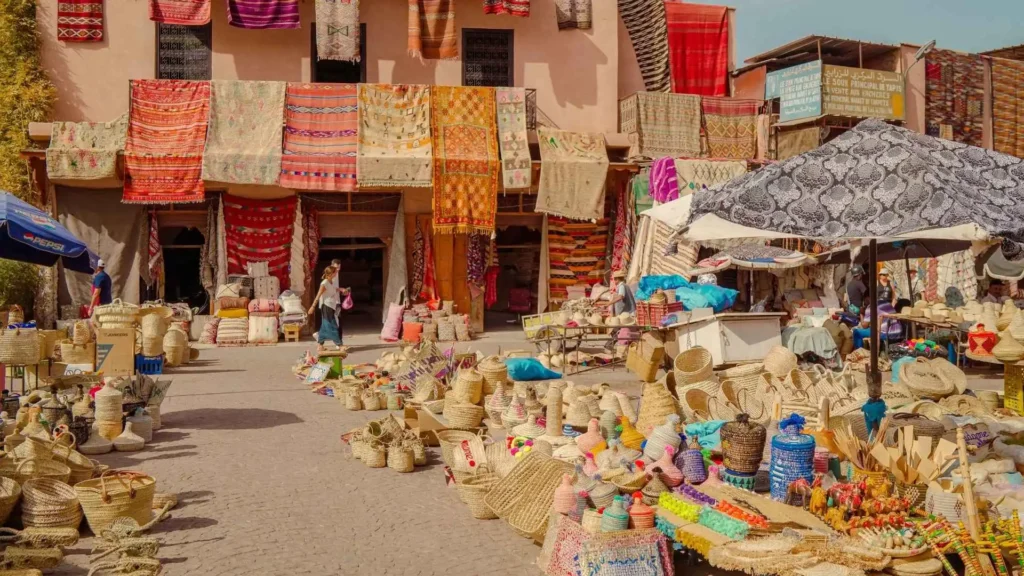 Straw baskets and woven bags displayed alongside Moroccan rugs at an open-air souk — handwoven bags are a popular pick for what to buy in Marrakech