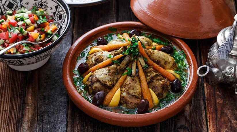 Moroccan food tagine with chicken, carrots, preserved lemon and black olives served in a traditional clay pot