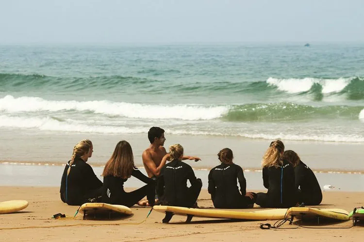 A local surf instructor coaching a group of beginners on the beach at a surf camp in Morocco near Taghazout